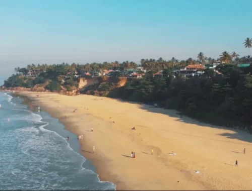 A lively day at Varkala Beach, Kerala, where people relax on the sand with a beautiful hill visible in the distance.