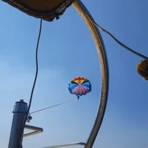 Parasailing adventure at Anjuna Beach, Goa, with a colorful parachute soaring in the clear blue sky, viewed from under the shade of a beach umbrella.