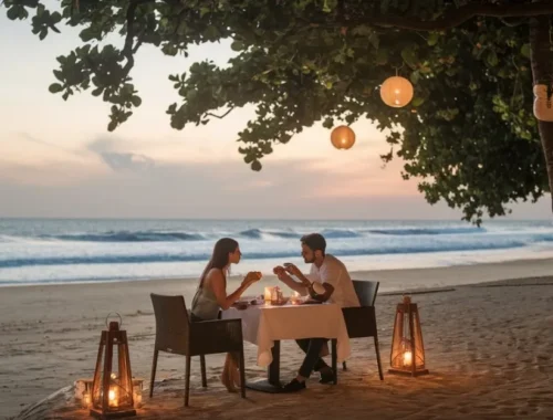 Romantic beachside dinner at sunset with a couple under lantern-lit tree, ocean waves in the background